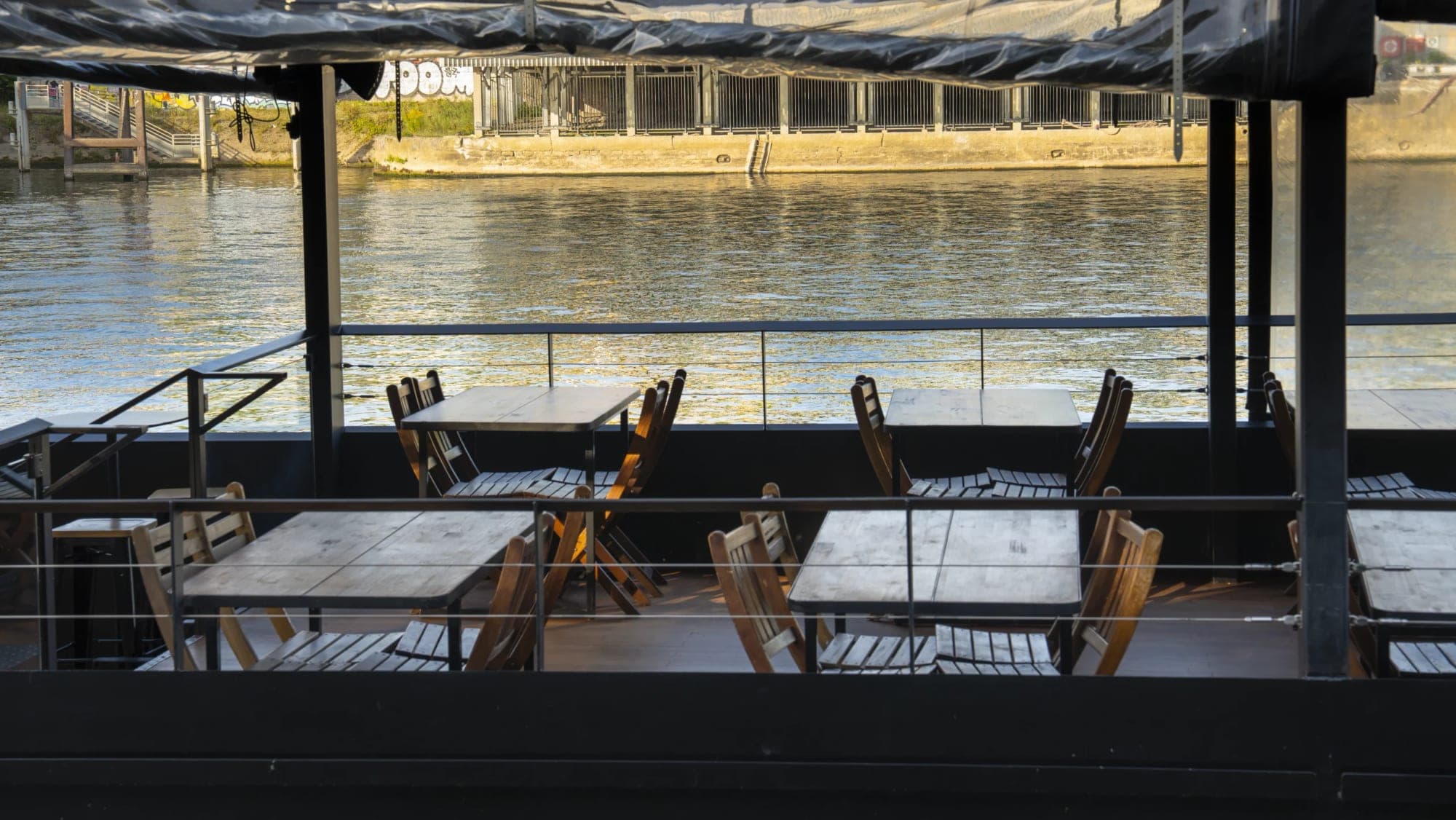 Outdoor seating area with tables and chairs on a deck by a river.
