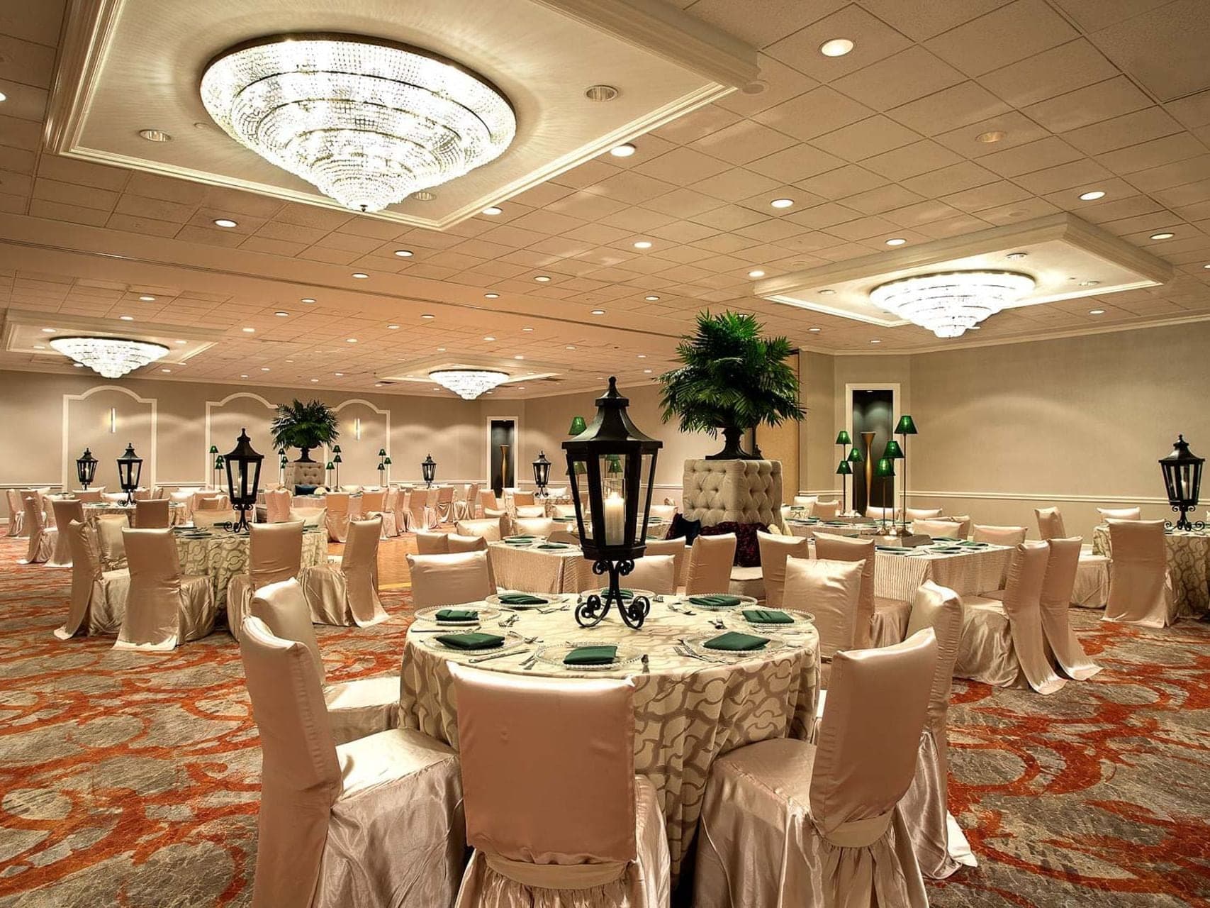 A reception hall with round tables set for a wedding and chandeliers.