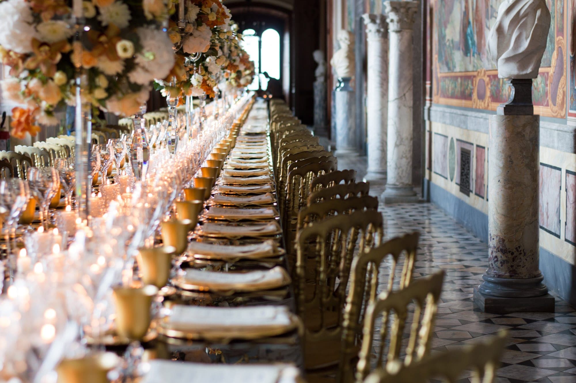 A long dining table set for a wedding reception with golden chairs and floral arrangements.