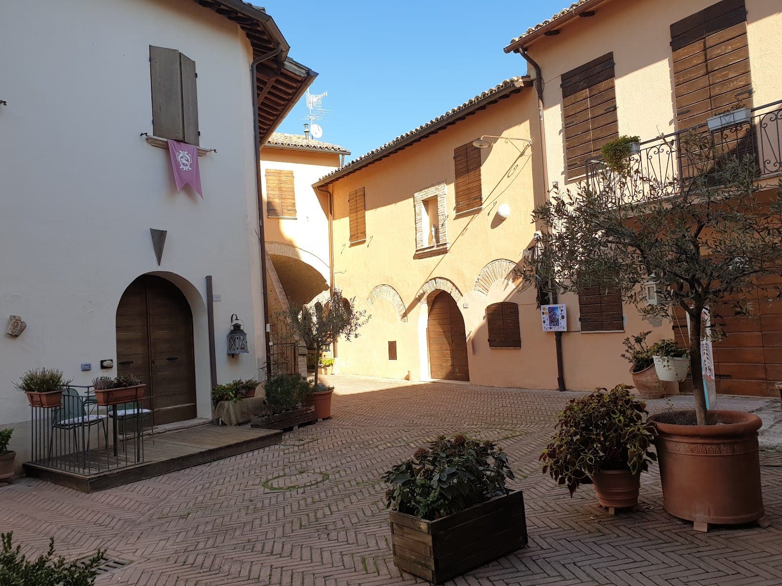 A paved courtyard with buildings and potted plants under a blue sky.
