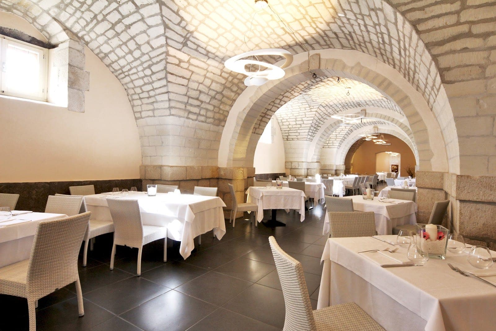 A reception dining room with stone arches and white tablecloths.