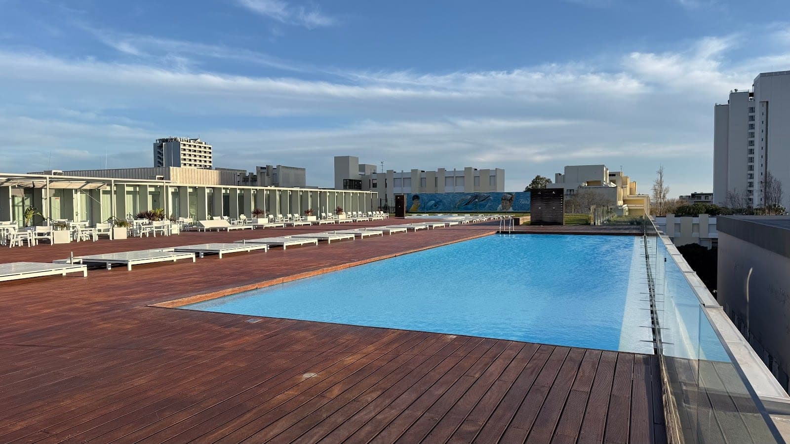 Rooftop swimming pool with wooden deck and lounge chairs.