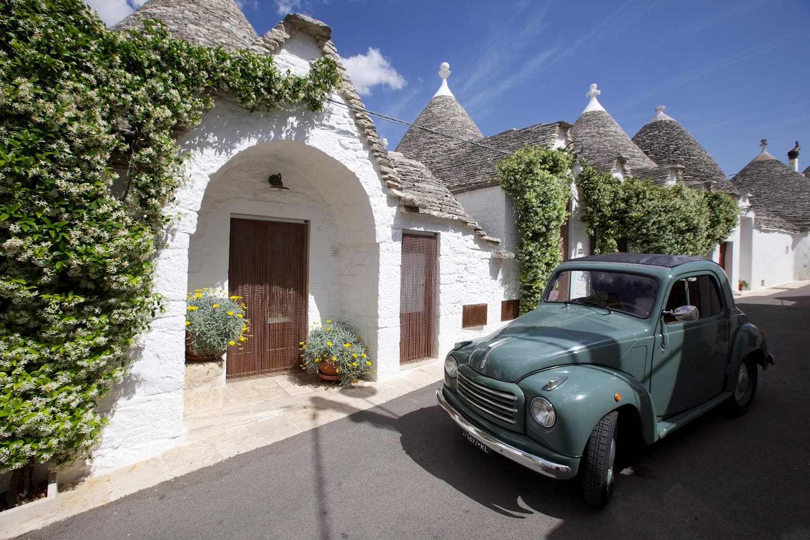 Exterior of white trulli buildings with a vintage car parked on the street.