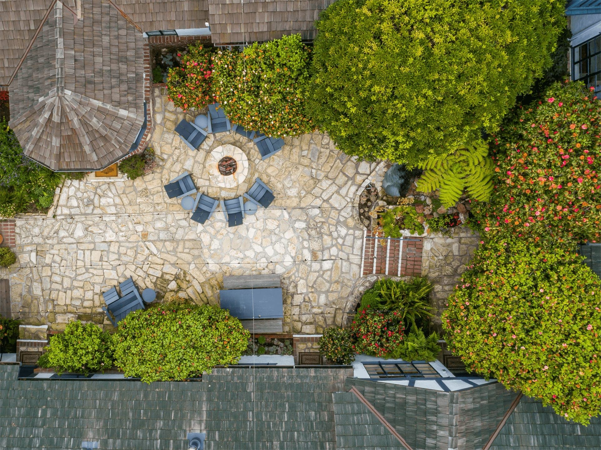 Aerial view of a stone patio with a fire pit and chairs surrounded by lush greenery.