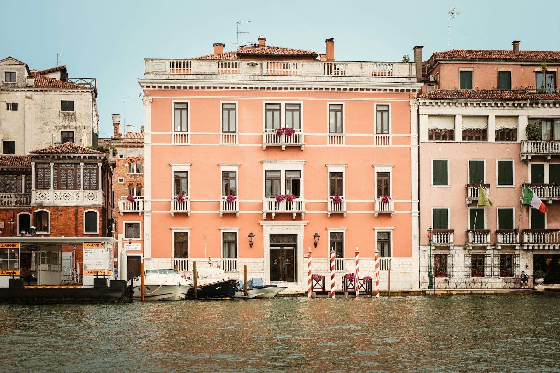Exterior of a pink building on a canal in Venice with boats.