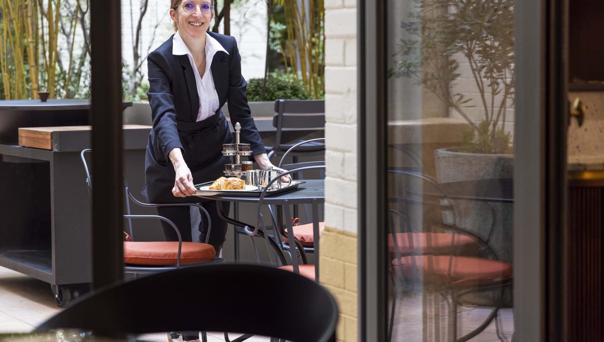 A waiter serves breakfast on a terrace with bamboo plants.