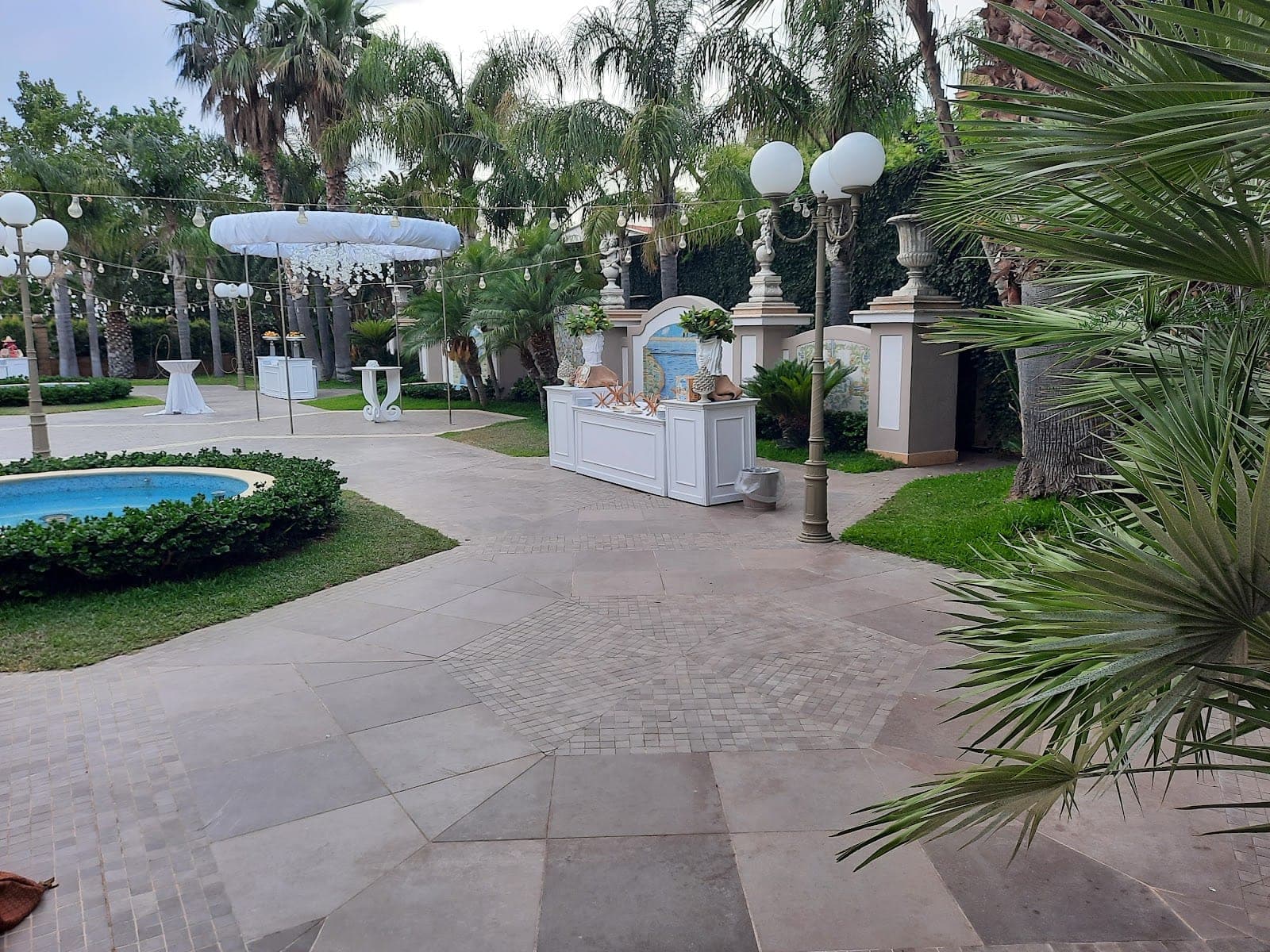 A garden with a fountain, bar, and tables set up for an event.