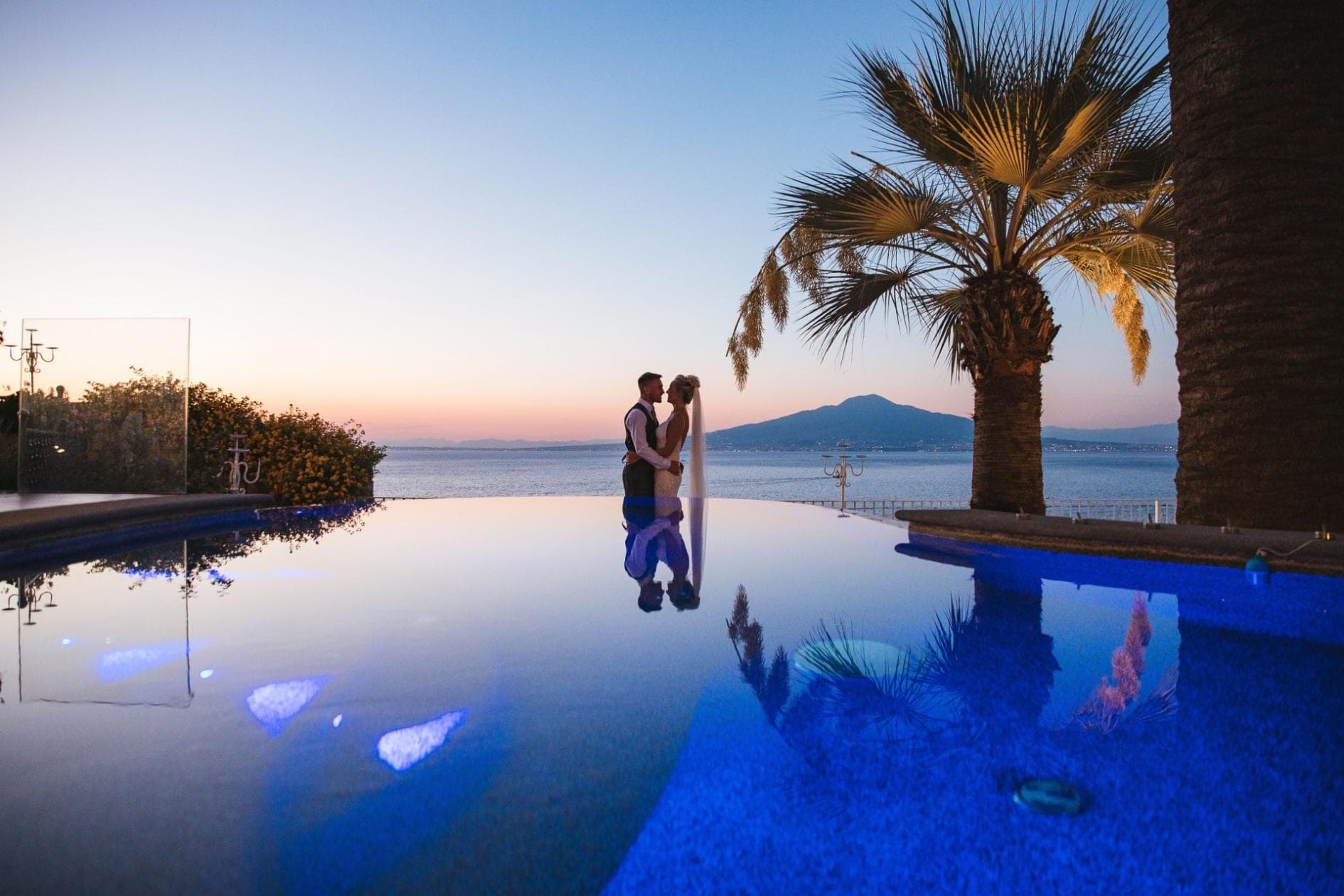 Couple by infinity pool with sea view and palm trees at sunset