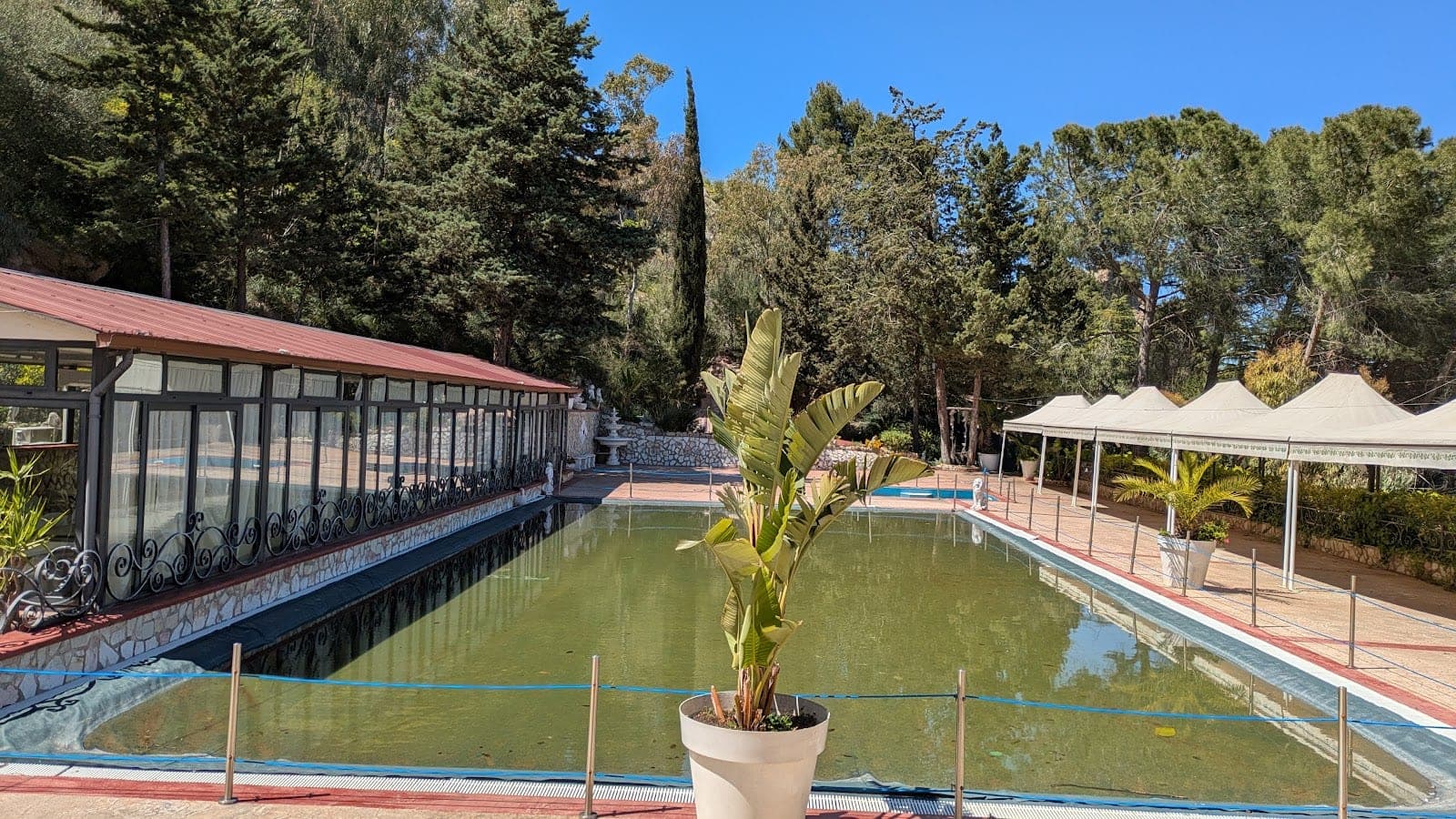 A swimming pool area with tents and a building surrounded by trees.