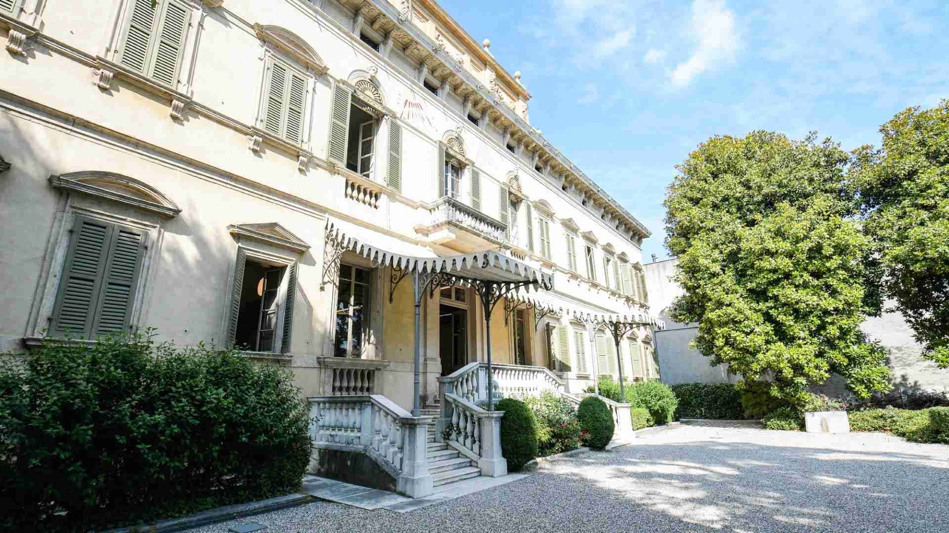 Exterior of a large, pale building with green shutters and a grand entrance.