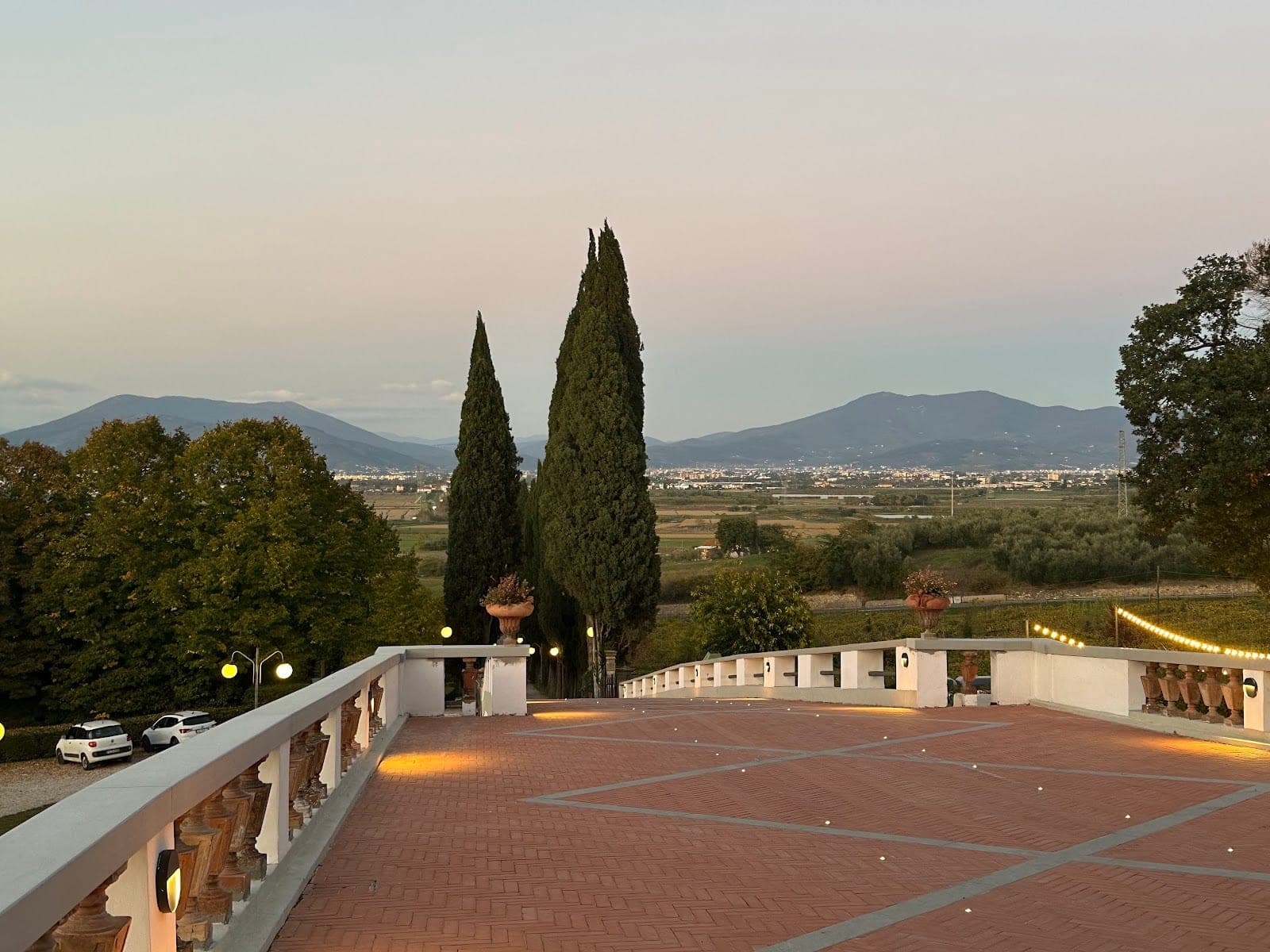 Terrace overlooking Tuscan countryside at dusk with cypress trees and distant lights.