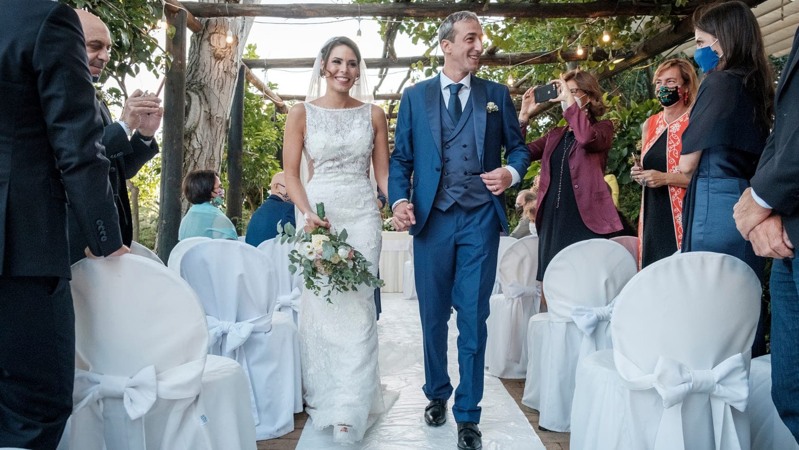 A bride and groom walk down an aisle at a wedding ceremony.