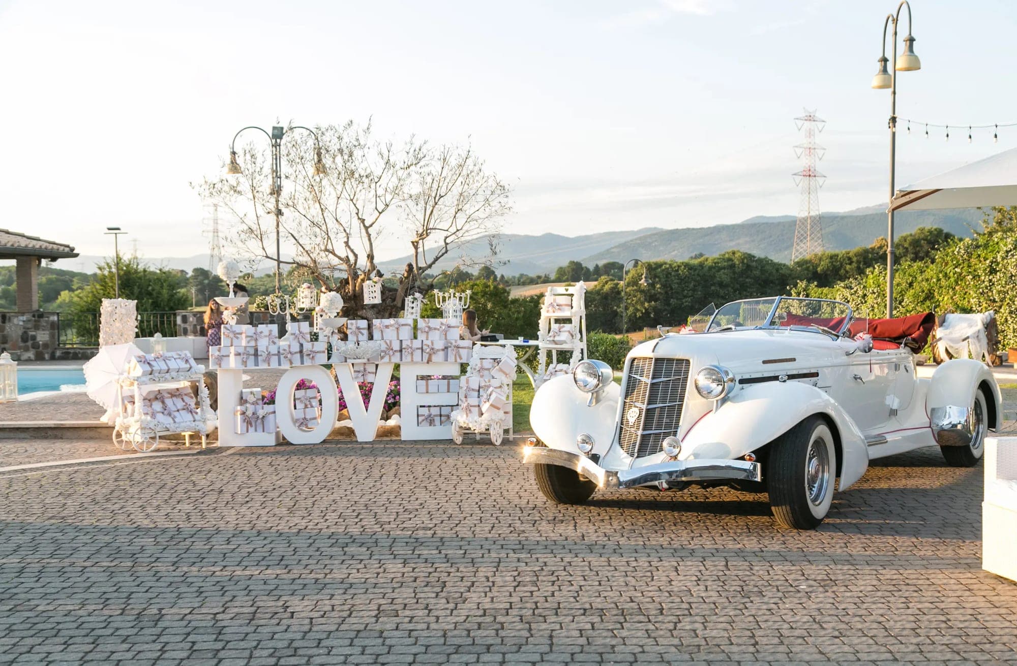A white vintage car parked next to large white LOVE letters and wedding favors.