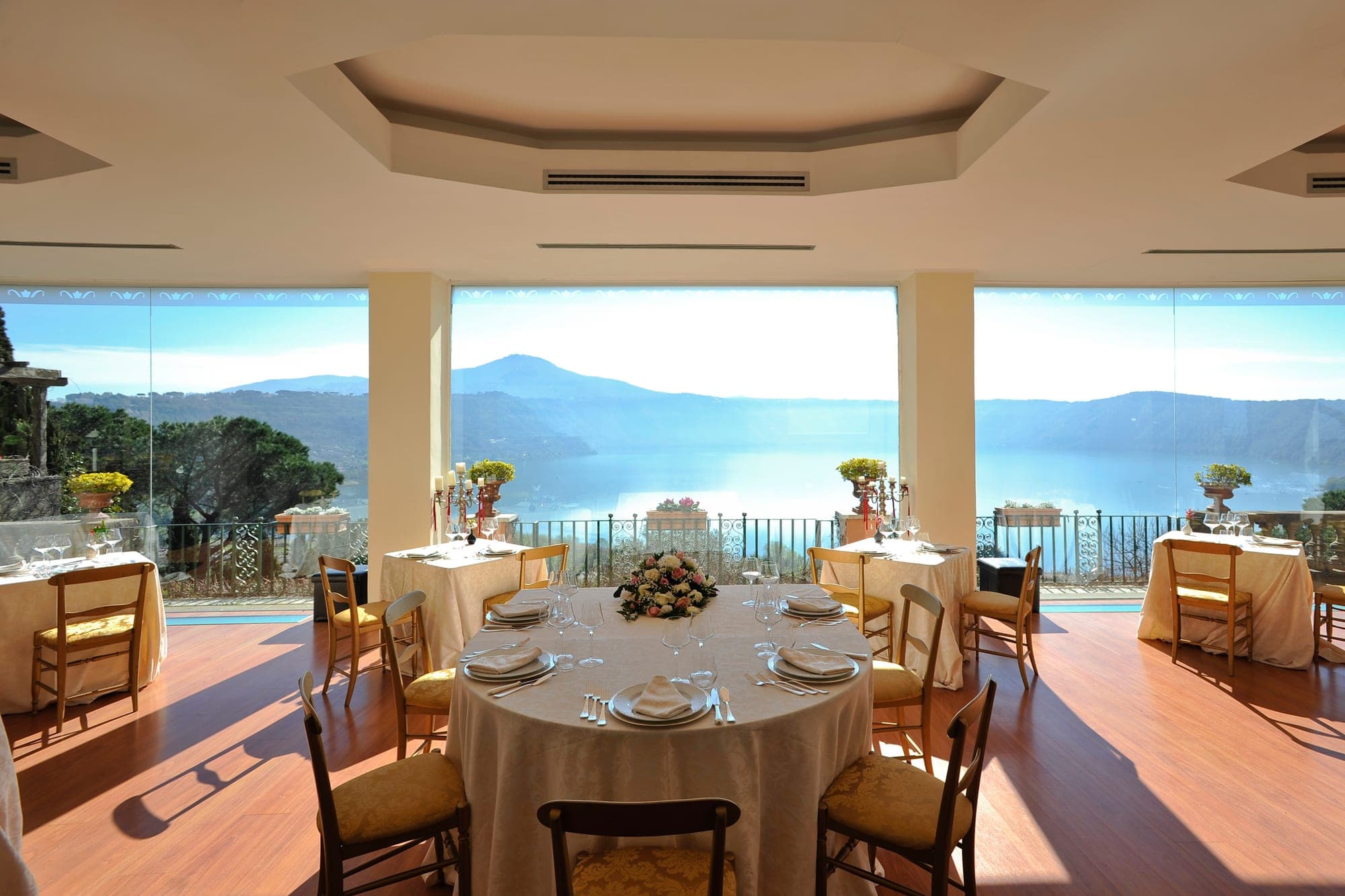 Dining room with tables set for a reception overlooking a lake and mountains.