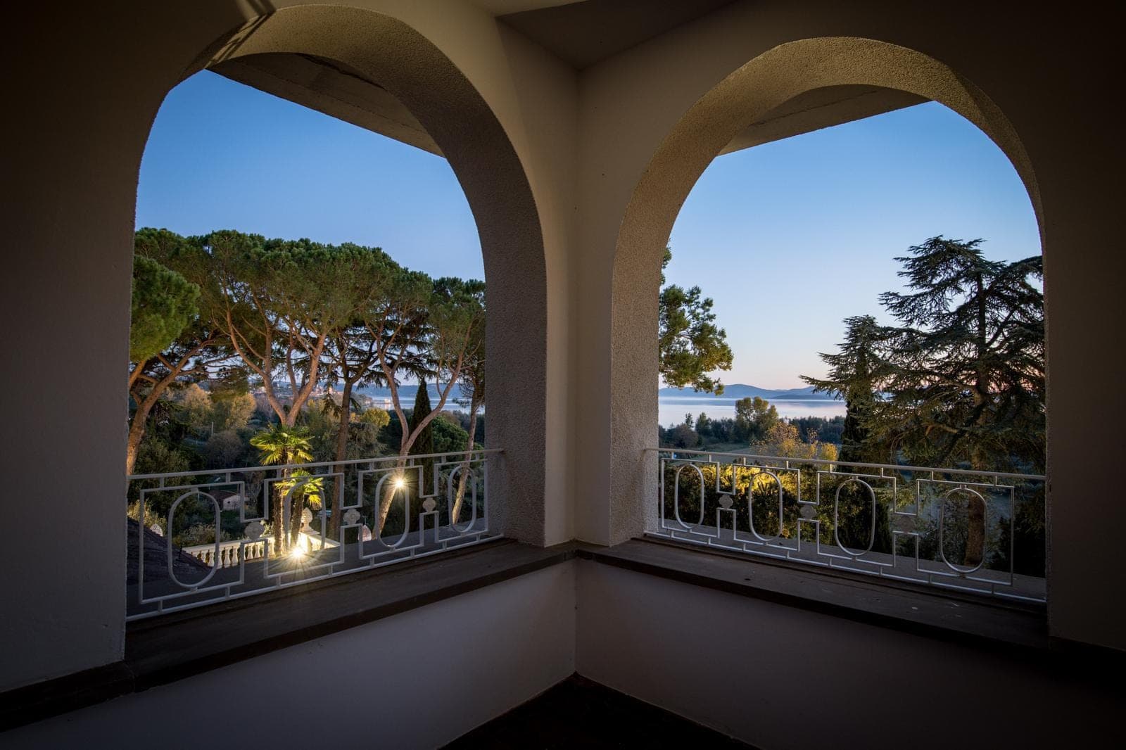 View of a lake and trees through arches from a balcony at dusk.