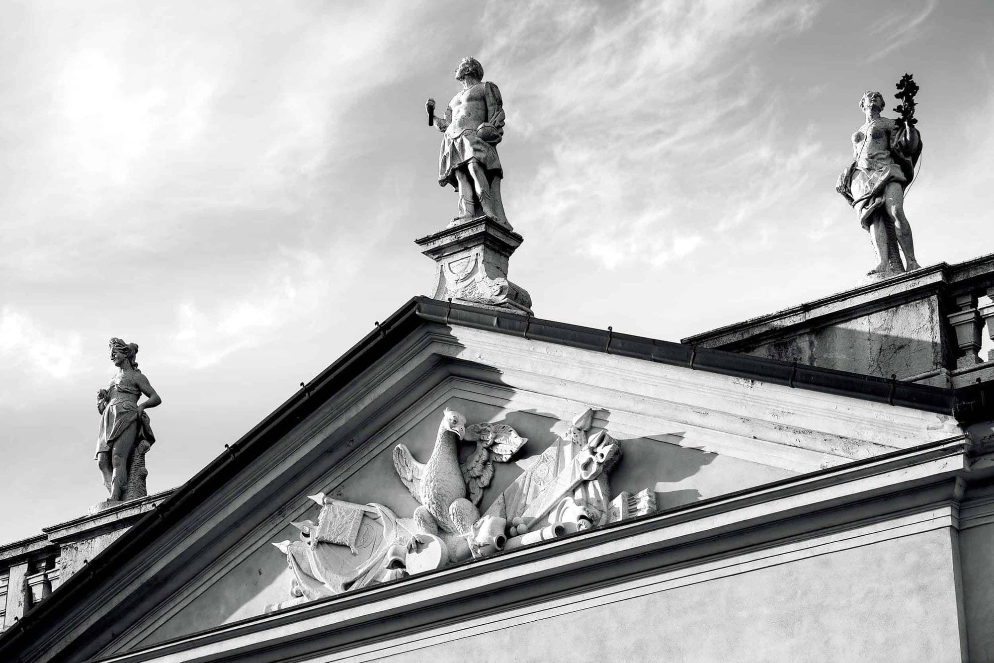 Statues adorn the roofline of a historic building against a cloudy sky.