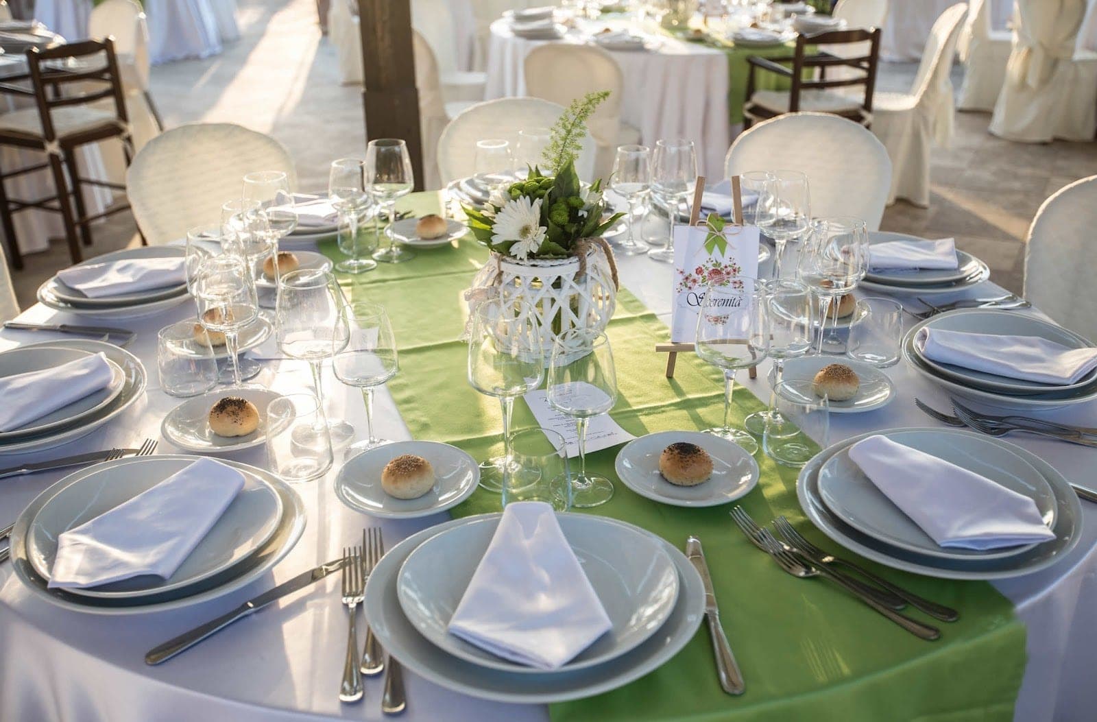 A wedding reception table is set with plates, cutlery, glasses, and a floral arrangement.