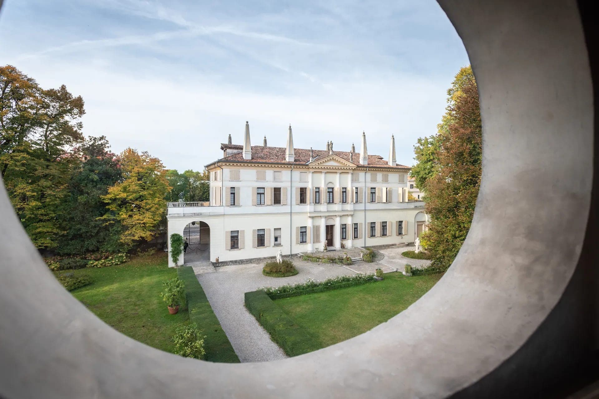 Exterior of a large white villa with a red tiled roof, viewed through a circular opening.