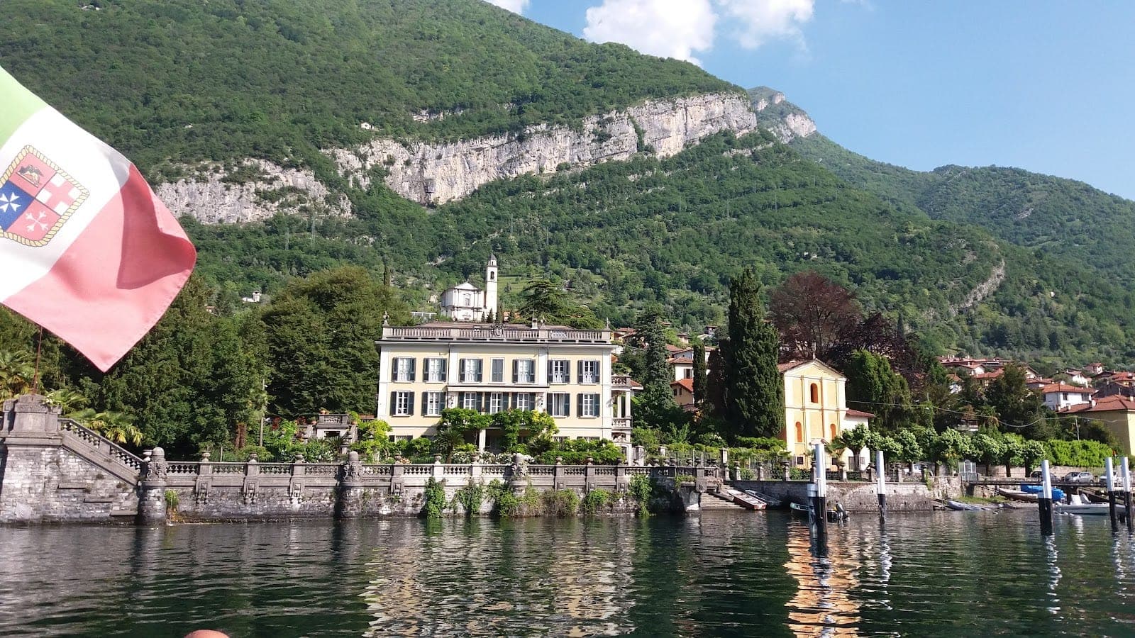 Villa Geno on a lake with a mountain behind it, and an Italian flag in the foreground.
