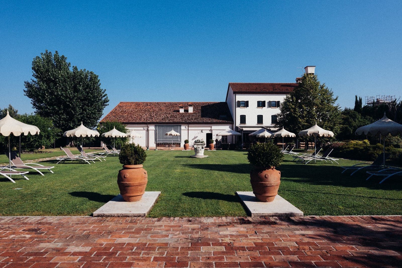 Lawn with lounge chairs and umbrellas in front of a white building with a red tile roof.