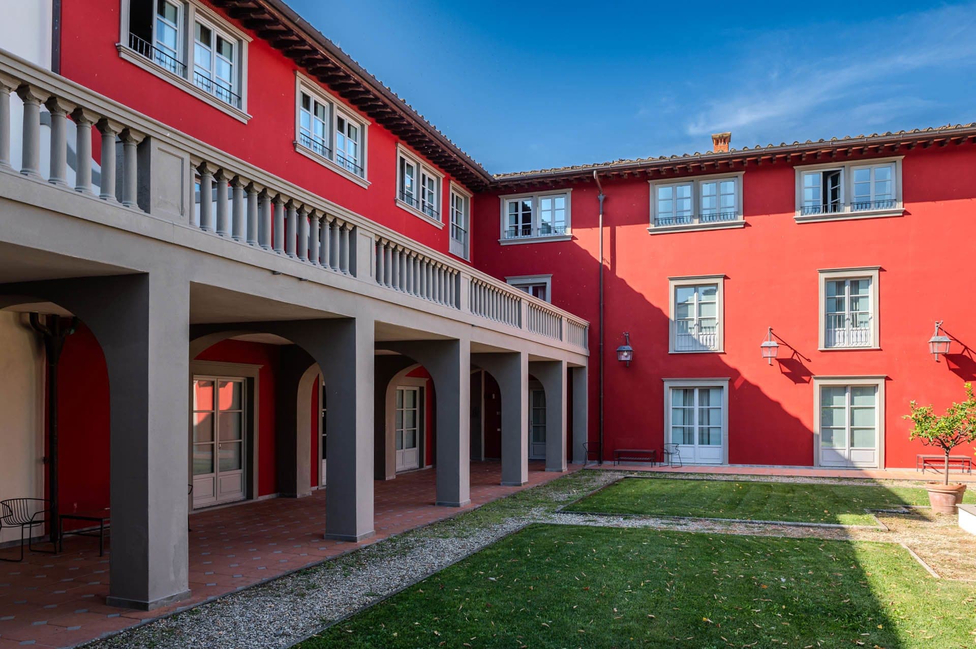 Courtyard of a red building with a balcony and a lawn.