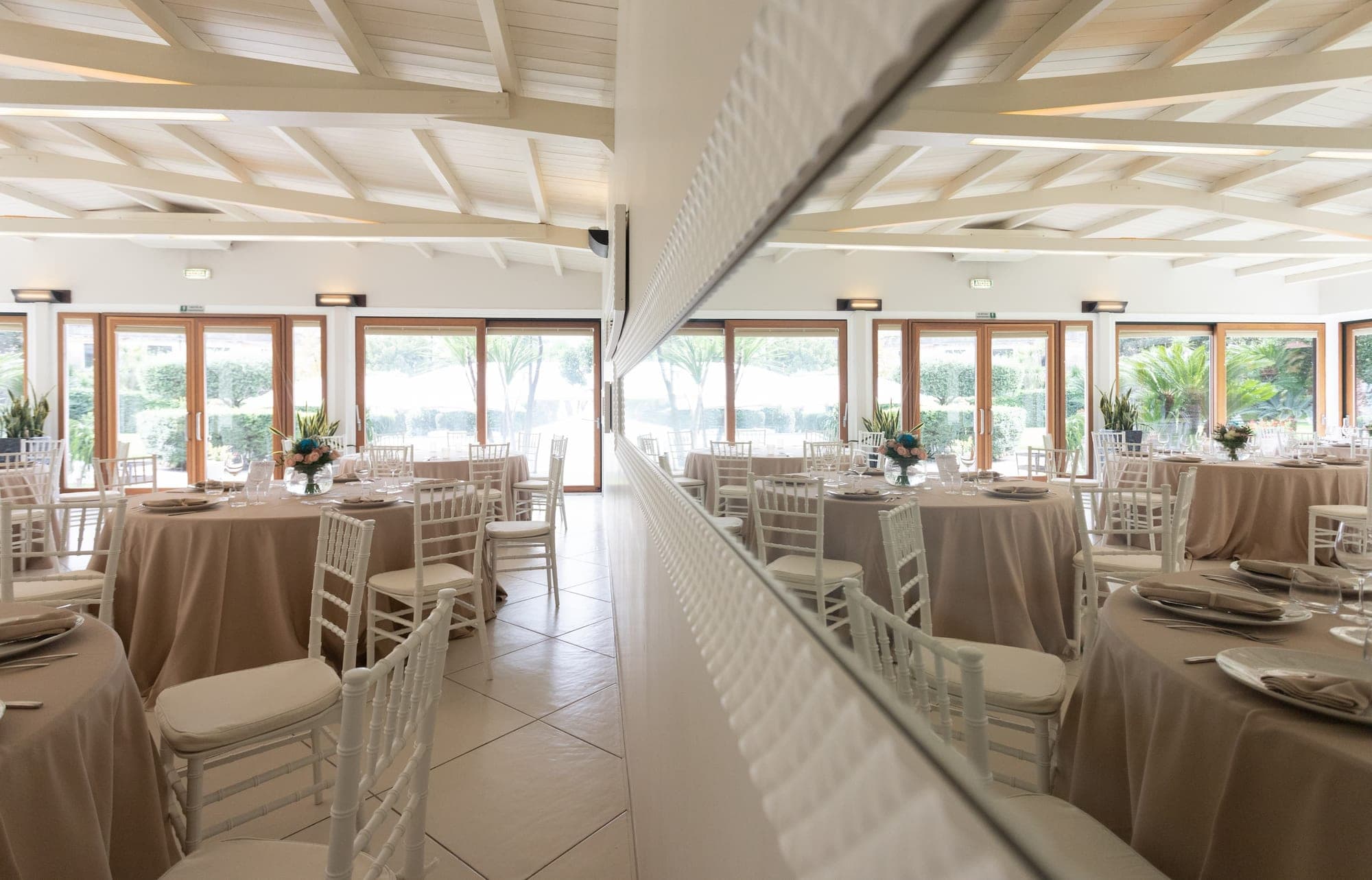 Reception room with round tables set for a wedding, large windows, and a mirror.
