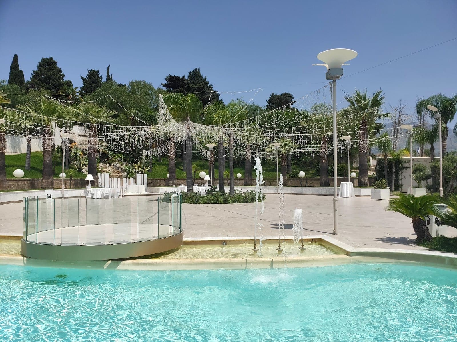 Outdoor area with fountains, palm trees, and string lights.