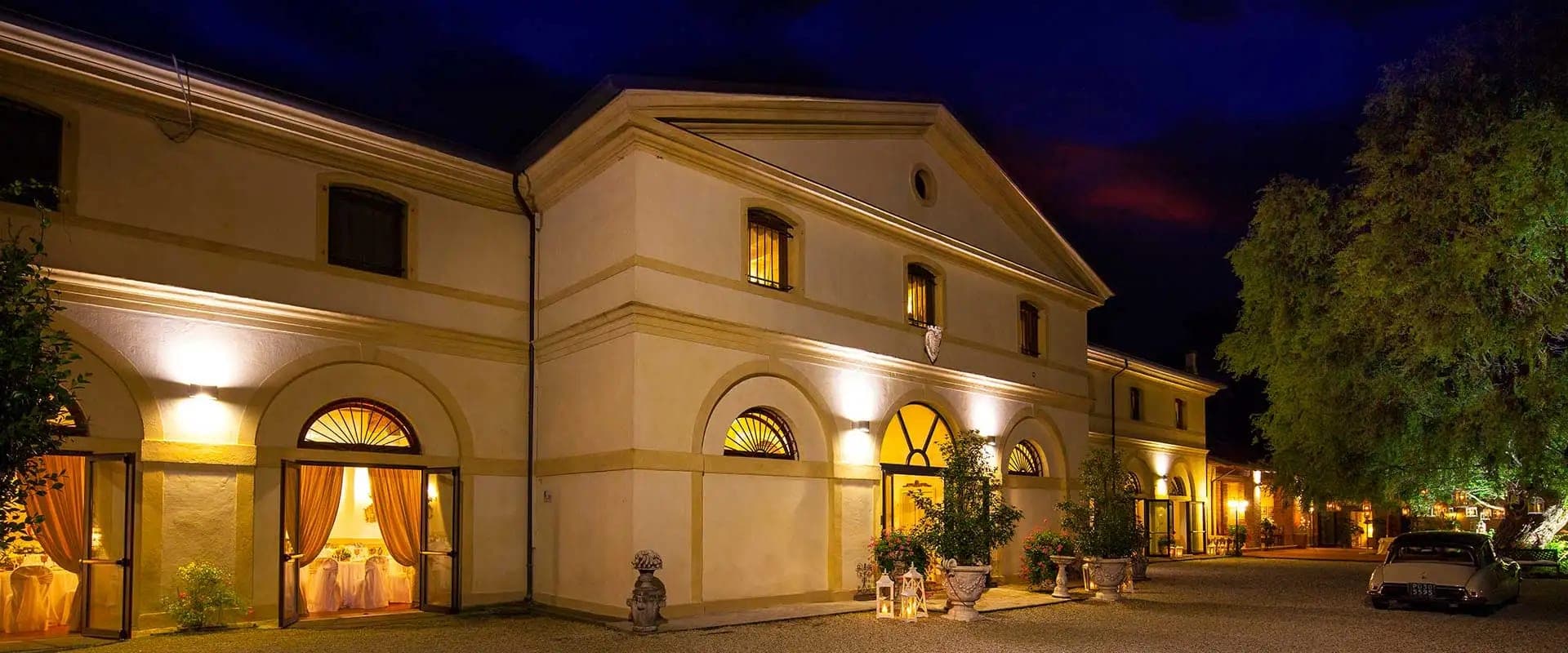 Exterior of a building at dusk with arched doorways and illuminated windows.