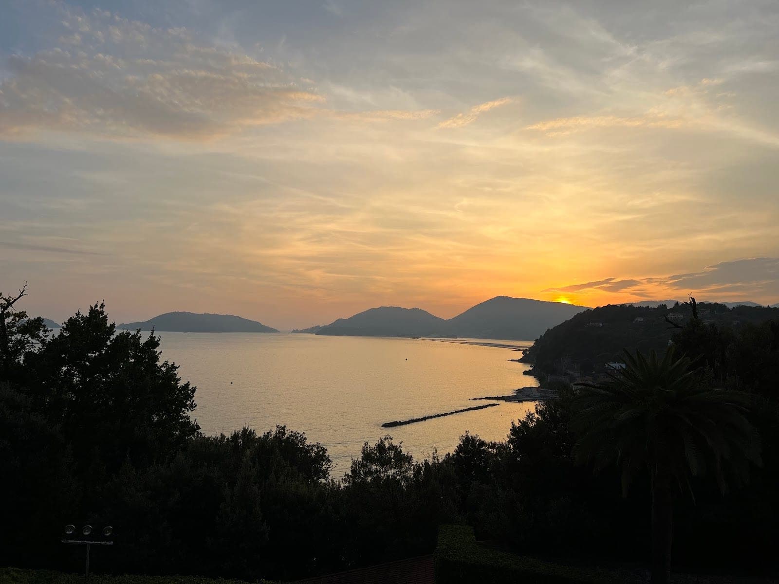 Sunset over the sea with hills and trees in the foreground.