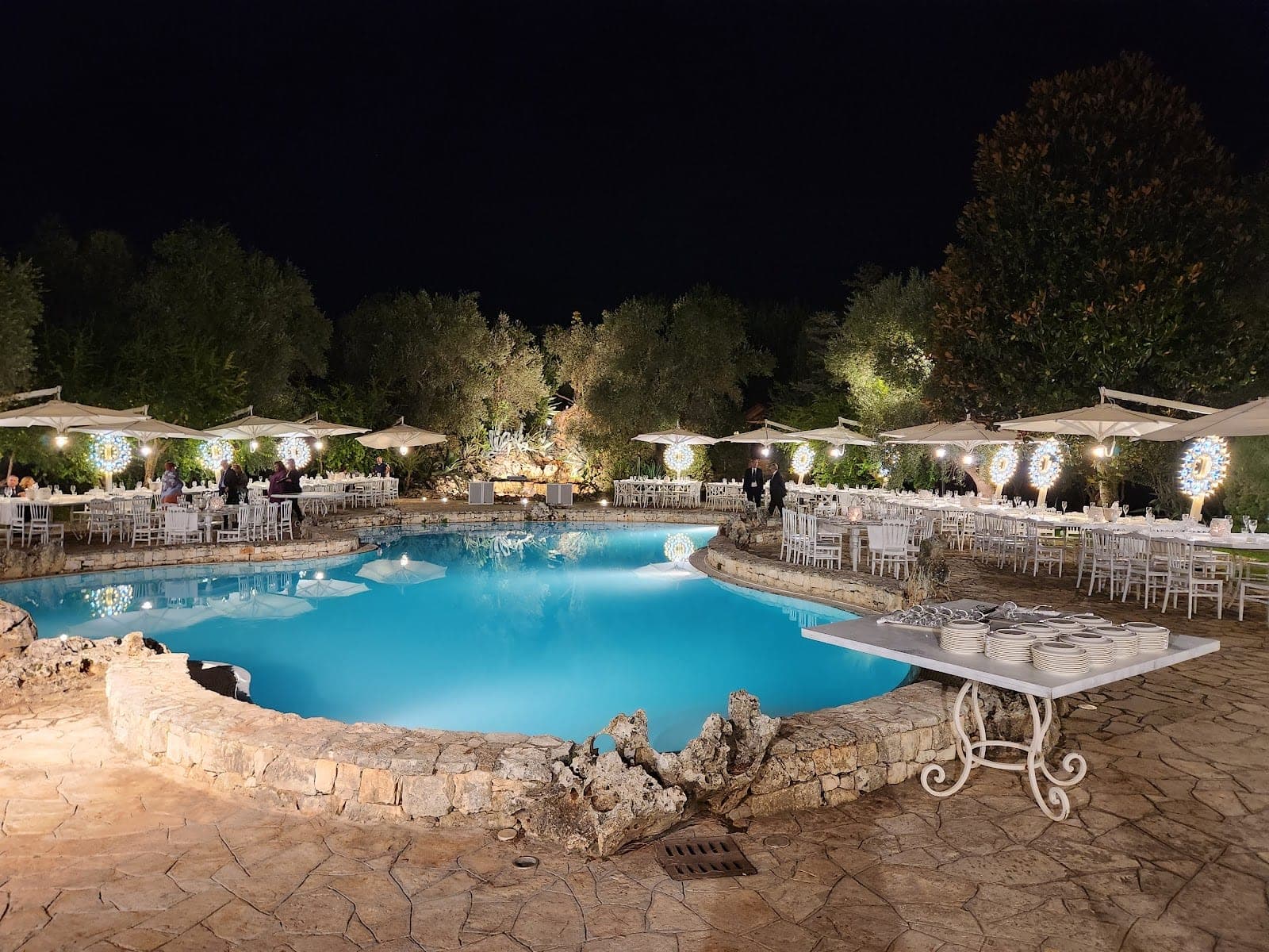 Outdoor reception area with a pool and tables set for guests at night.