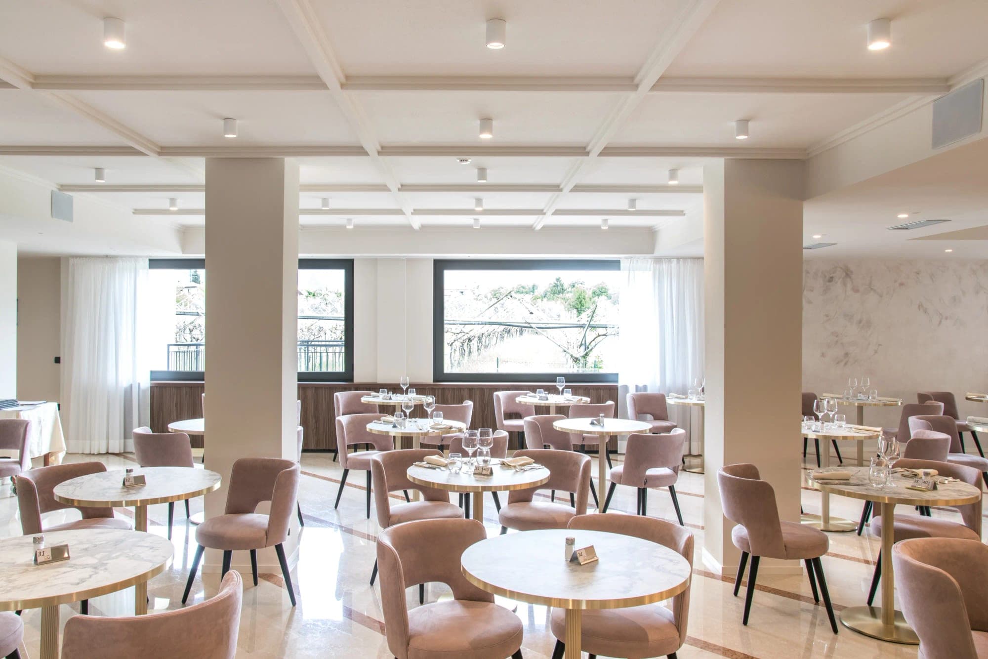 Dining room with pink chairs and marble-topped tables set for a reception.