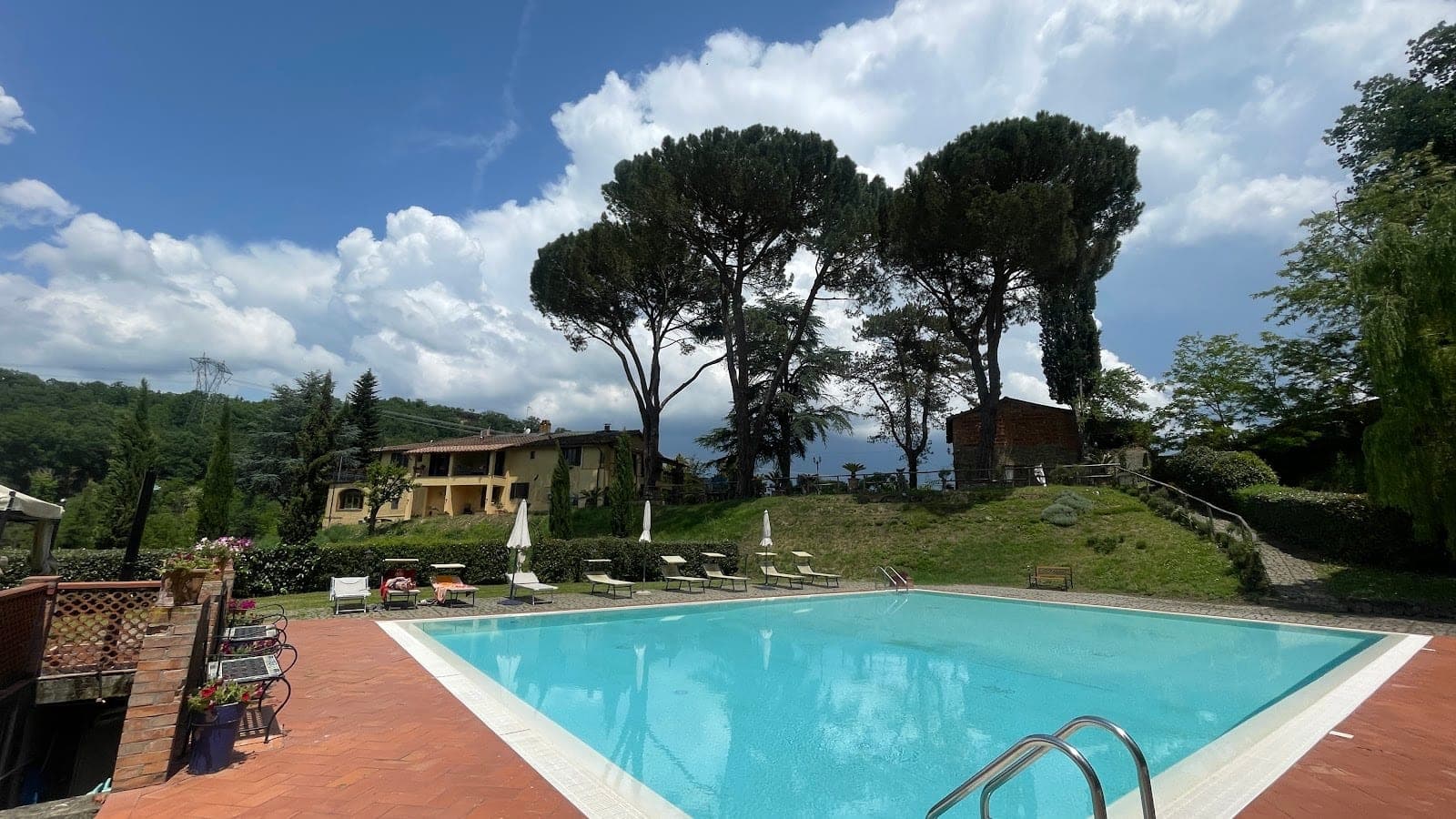 Swimming pool and grounds of a villa with trees and lounge chairs.