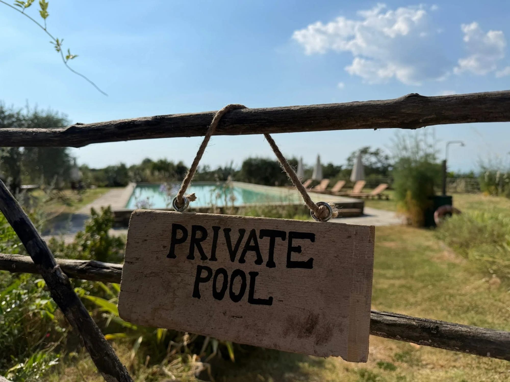 A wooden sign reading "PRIVATE POOL" hangs in front of a swimming pool and lounge chairs.