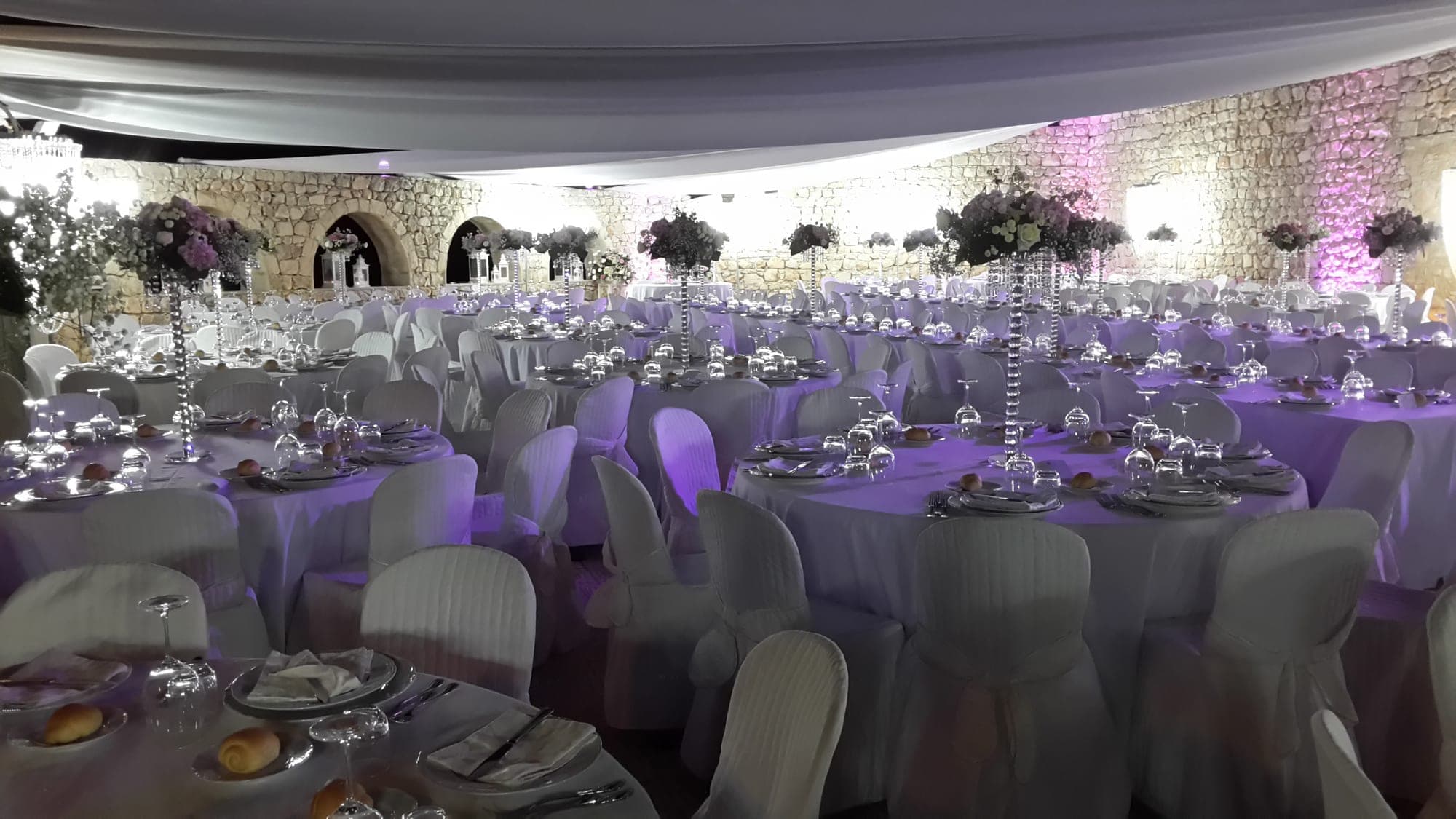A reception hall with many tables set for a wedding, decorated with flowers.