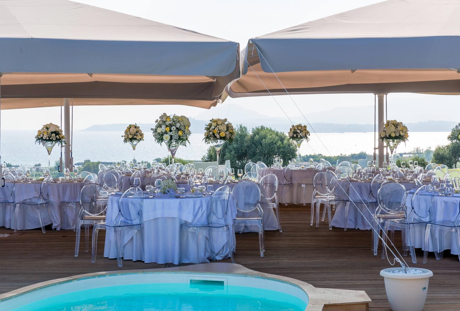 Tables set for a wedding reception on a wooden deck overlooking the sea.