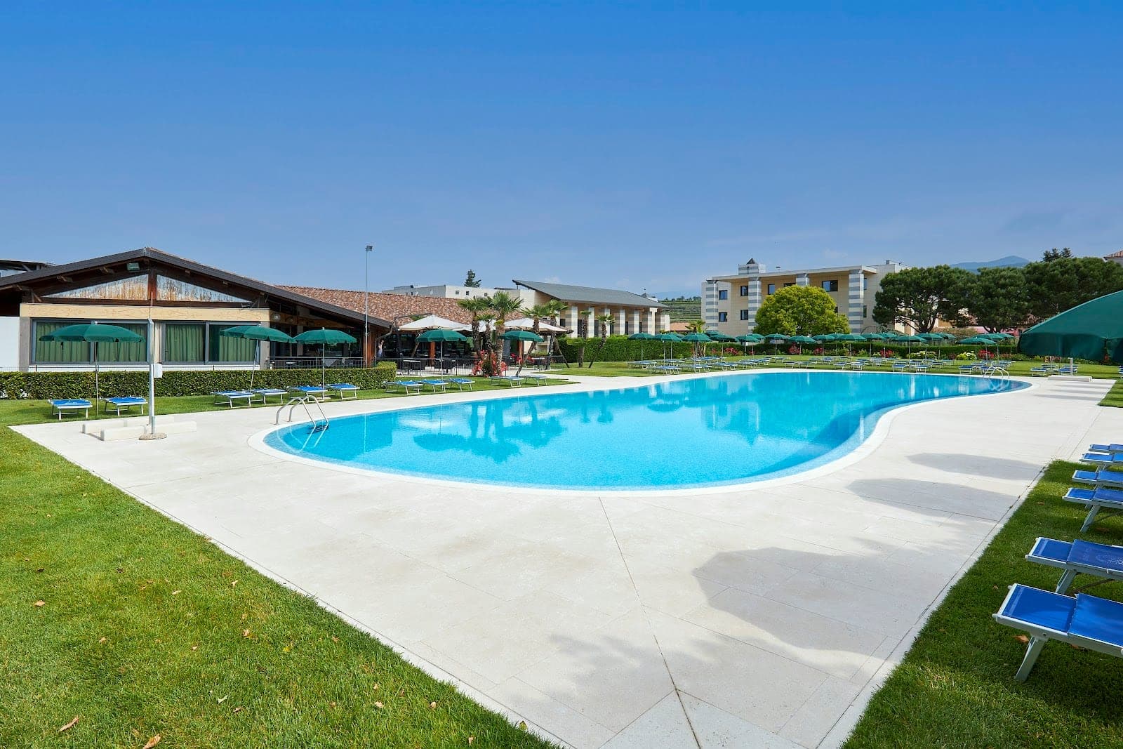 A large swimming pool with blue lounge chairs and green umbrellas on a sunny day.