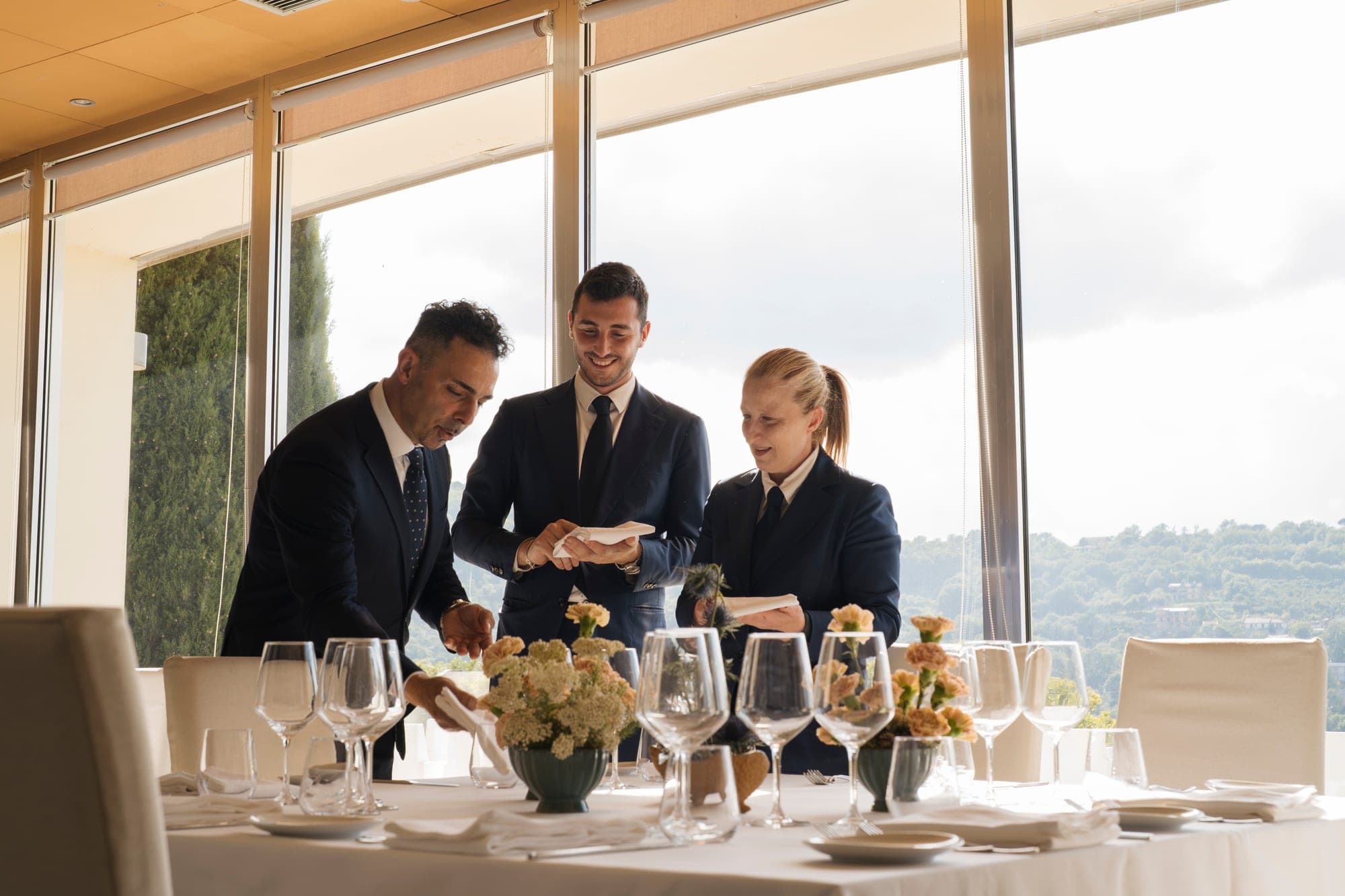 Staff setting a reception table with a view of rolling hills.