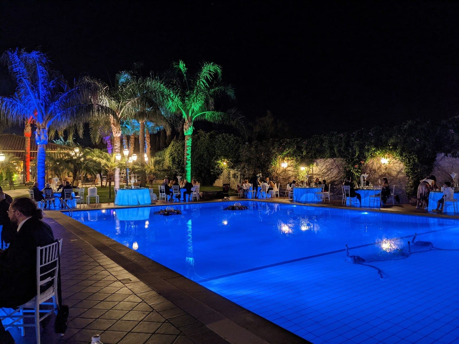 A swimming pool at night with tables set for a reception around it.