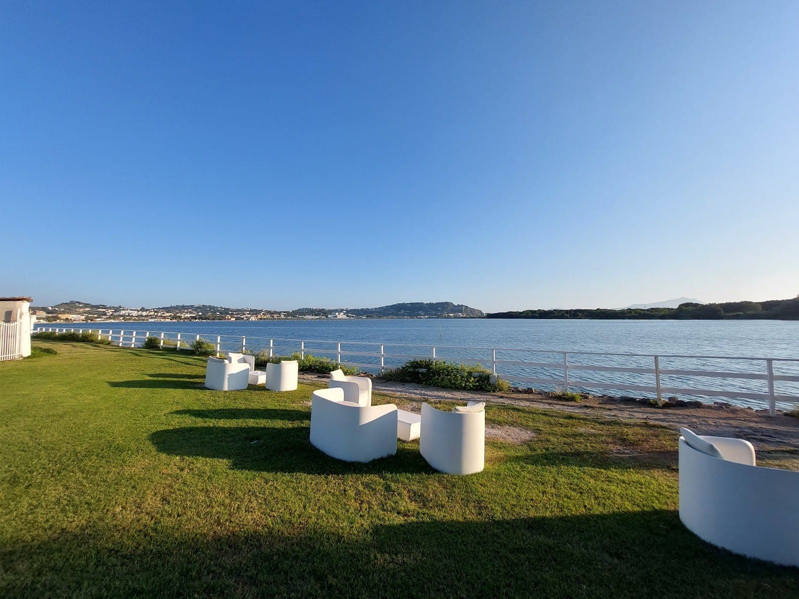 Lawn with white seating and a view of the water and distant town.