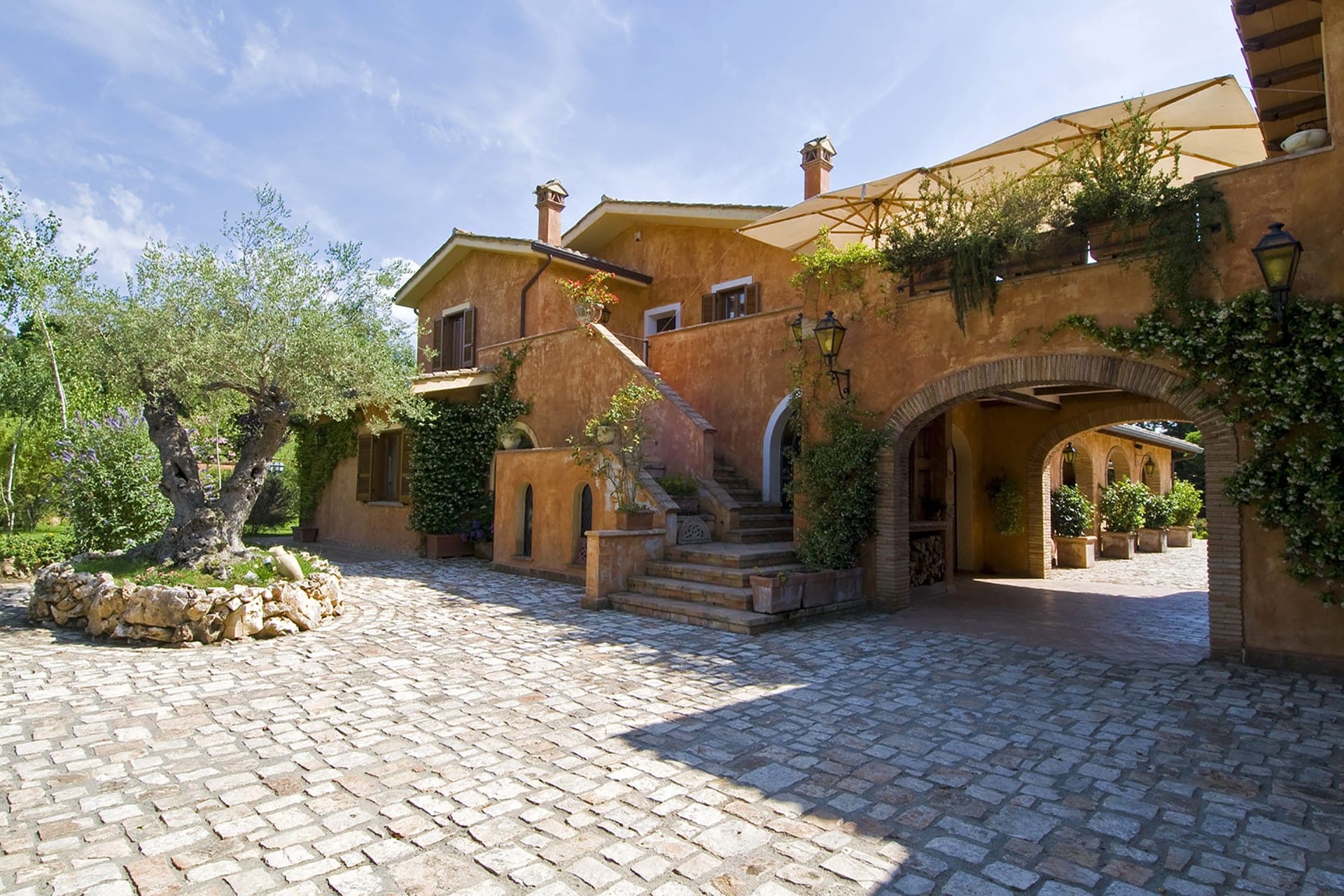 Exterior of Villa San Nicola with a cobblestone courtyard and an olive tree.
