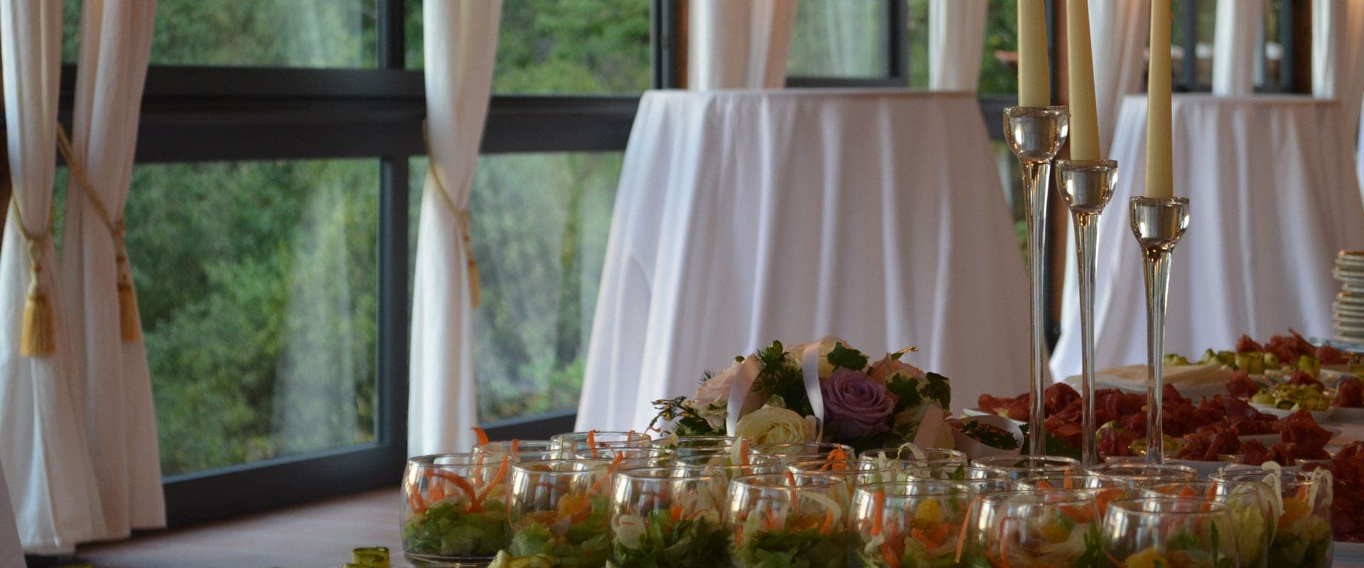 A reception table with appetizers, floral arrangements, and candles.