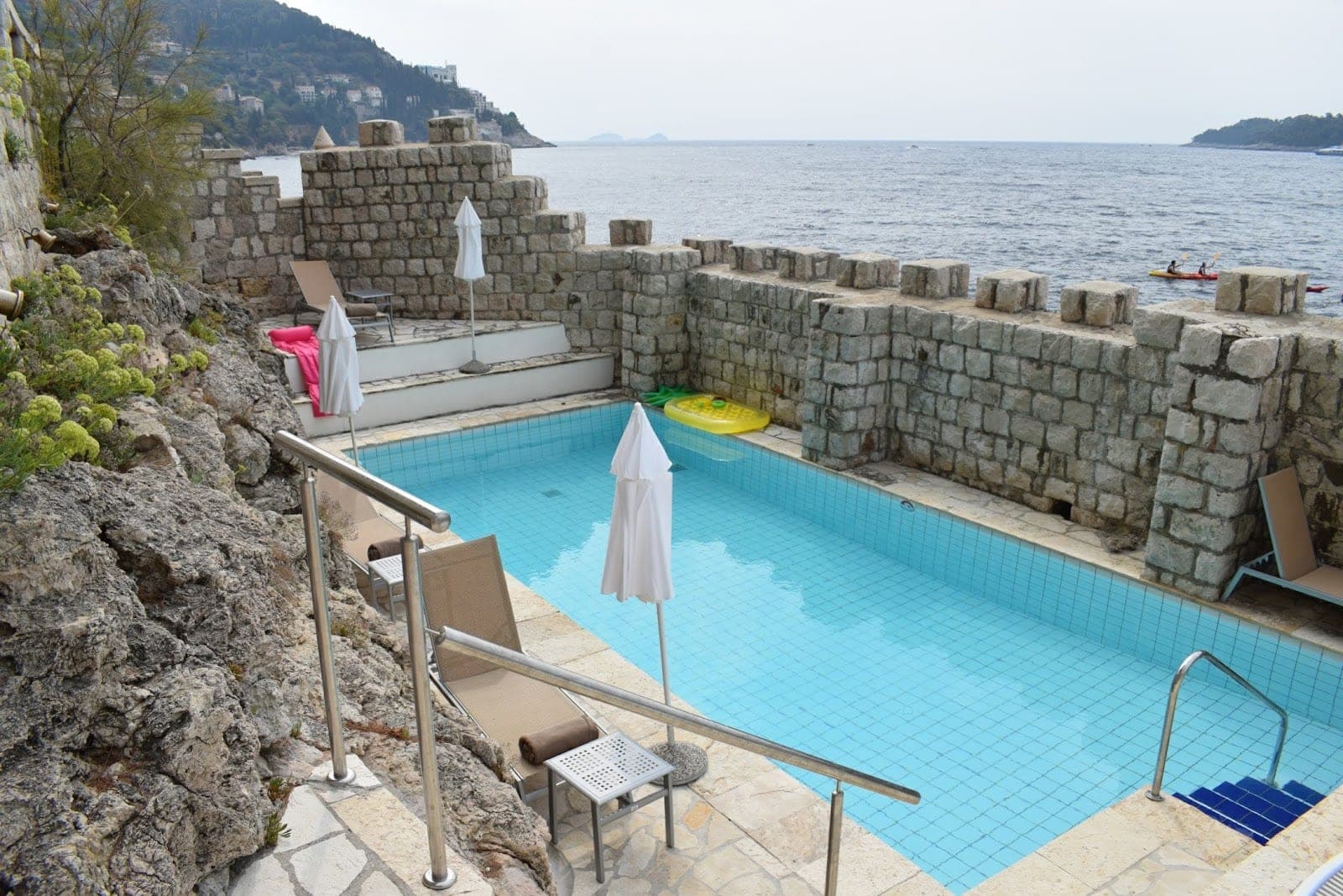 Swimming pool with stone walls and sea view.