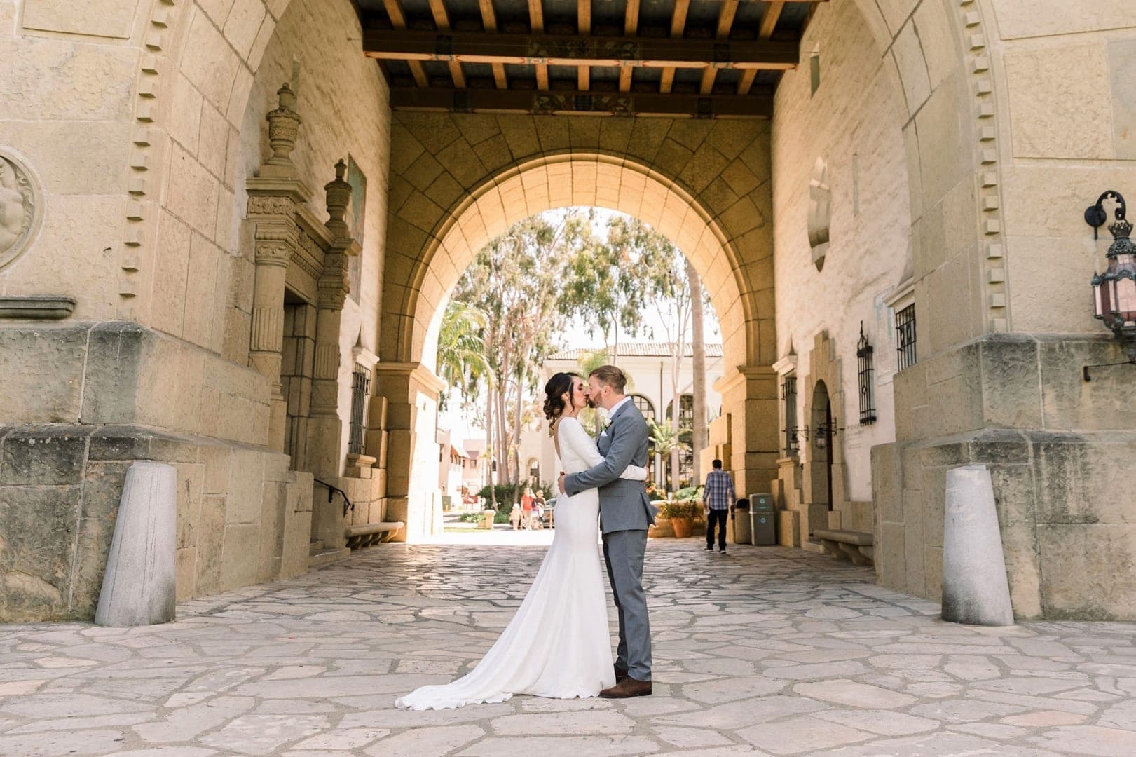 A bride and groom kiss under a stone archway at a wedding venue.