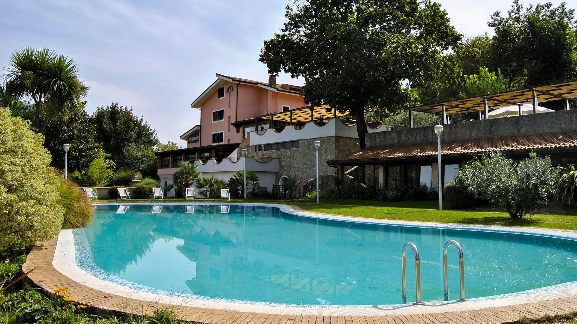 A swimming pool with steps in the foreground and a building with trees in the background.