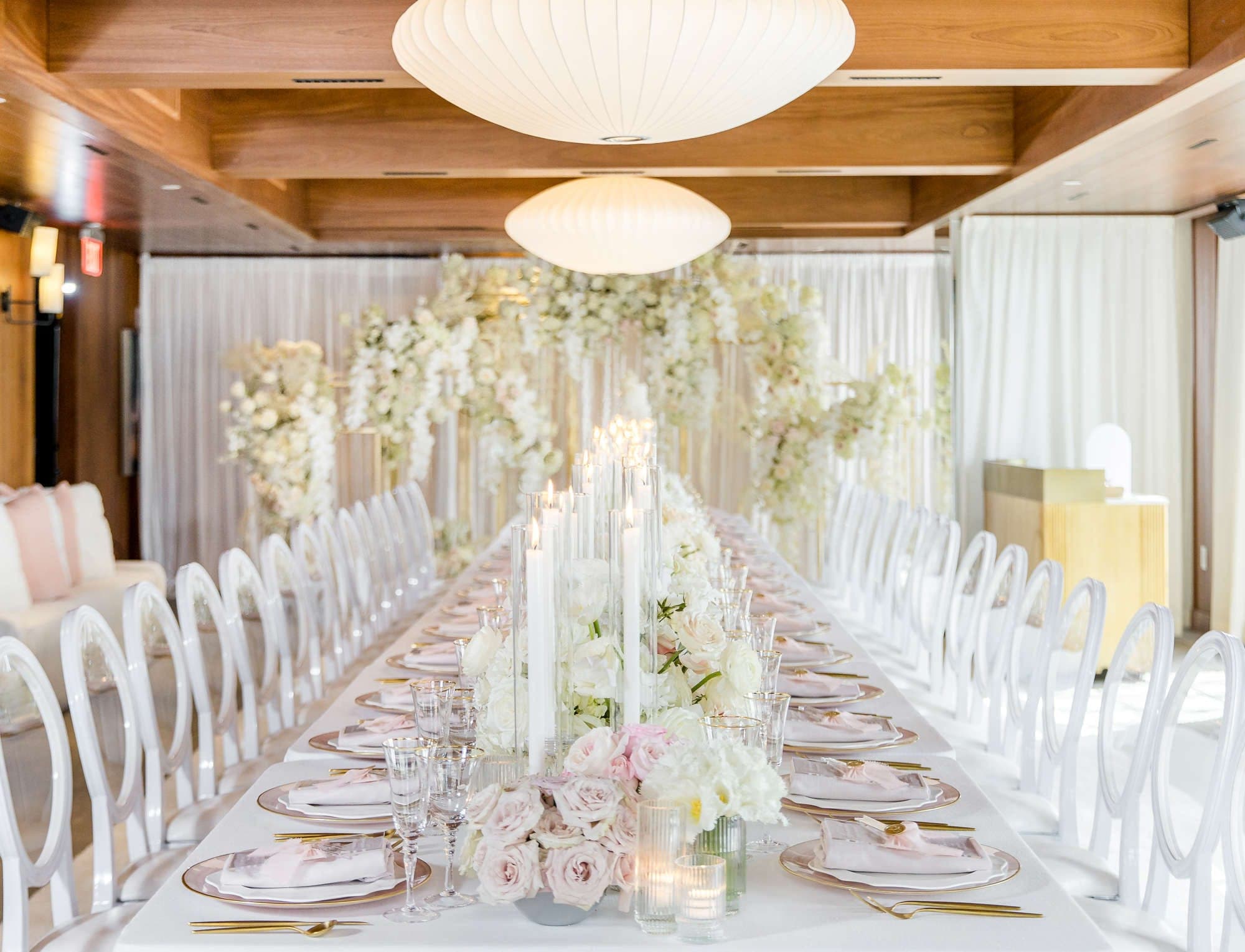 A long dining table set for a wedding reception with floral arrangements and white chairs.