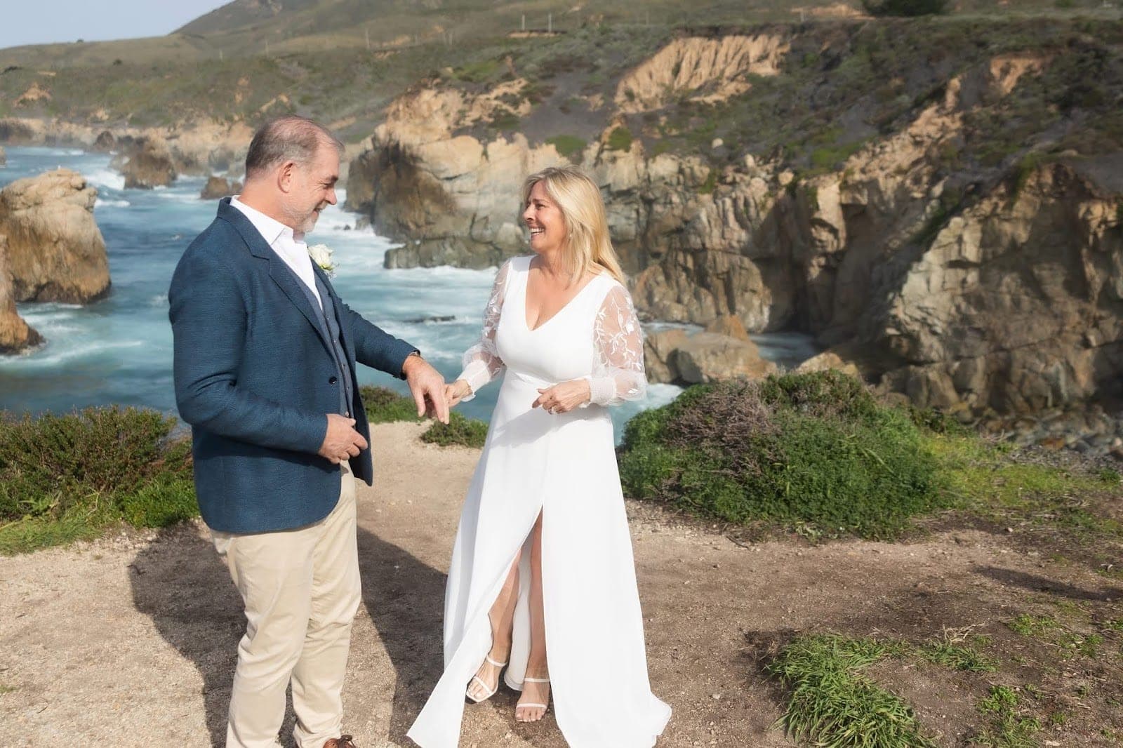 A couple stands on a cliff overlooking the ocean.