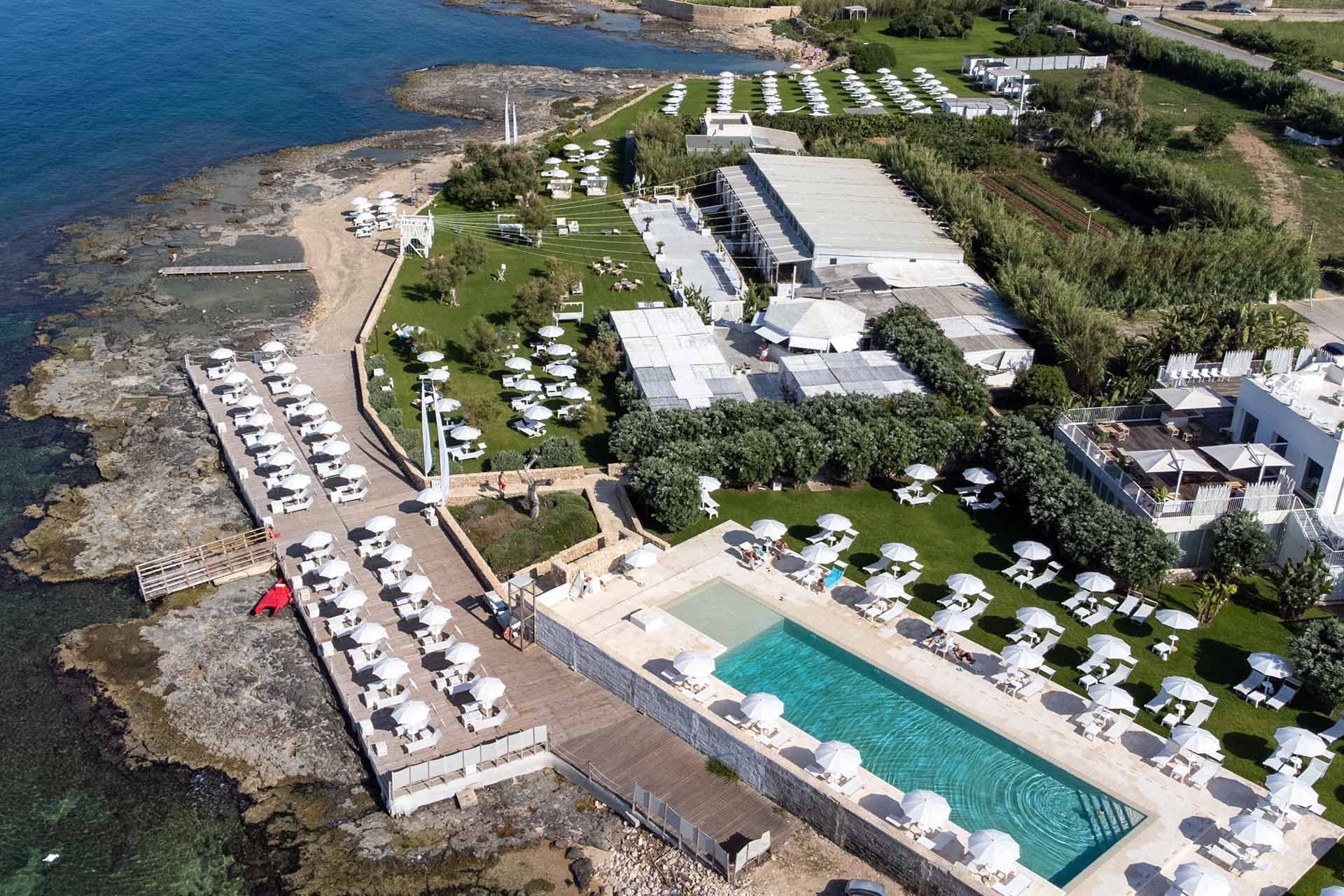 Aerial view of a beach club with a pool, pier, and outdoor seating.