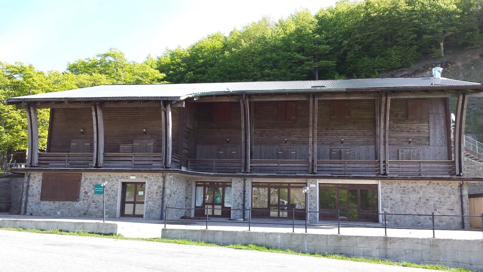 Exterior of a wooden and stone building with balconies and trees behind.